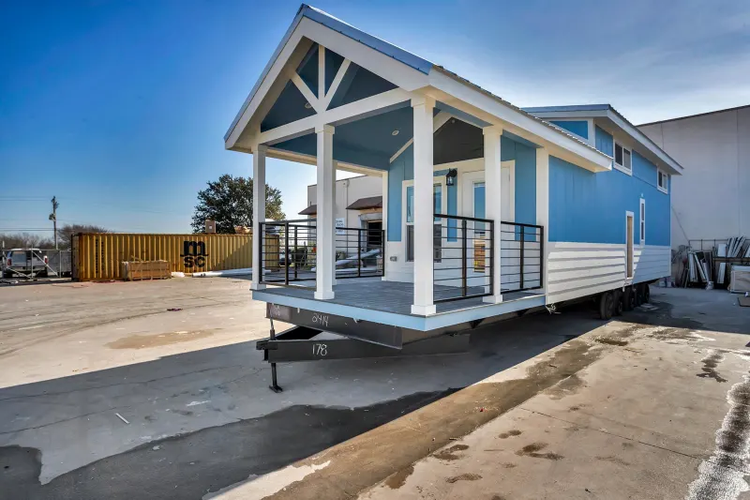 A tiny home sits on a trailer with a porch.