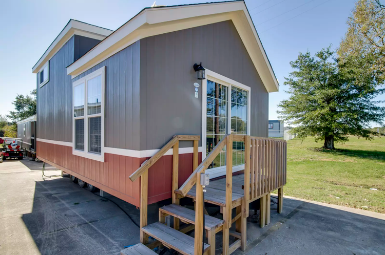 A tiny home with stairs leading up to a small deck and double door entrance.