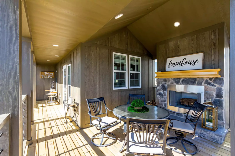 A tiny home with a large wrap around porch and a seating area near an outdoor fireplace.